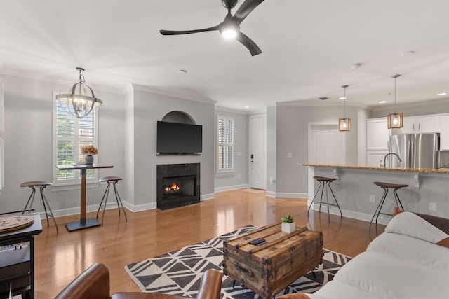 living room with ceiling fan with notable chandelier, light wood-type flooring, crown molding, and a wealth of natural light