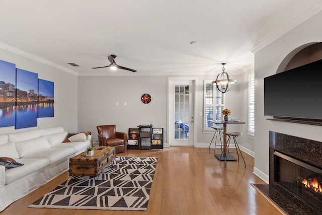 living room featuring a fireplace, wood-type flooring, ornamental molding, and ceiling fan with notable chandelier