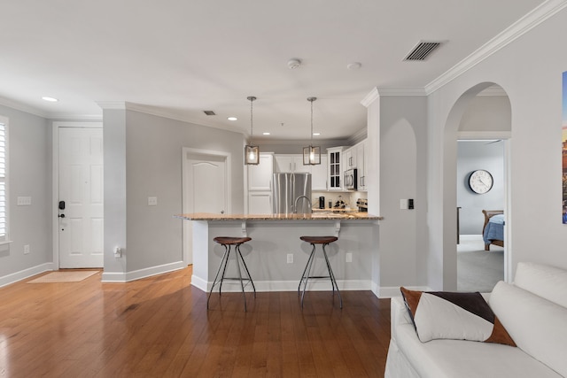 kitchen with wood-type flooring, decorative light fixtures, kitchen peninsula, appliances with stainless steel finishes, and white cabinetry