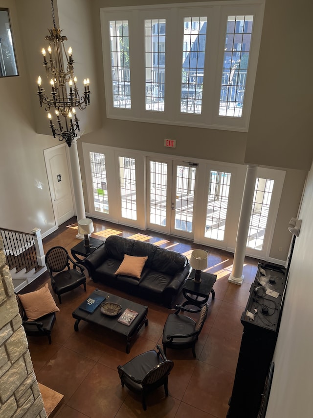 living room with a towering ceiling, decorative columns, dark tile patterned floors, and a chandelier