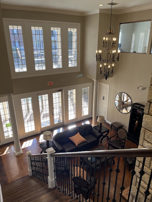 living room featuring ornamental molding, a chandelier, a towering ceiling, ornate columns, and dark hardwood / wood-style flooring