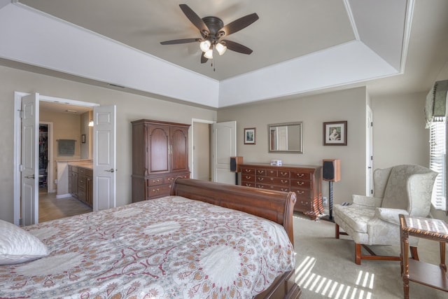 carpeted bedroom featuring ensuite bath, ceiling fan, and a tray ceiling