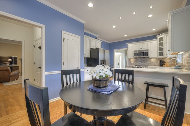 dining room with sink, ornamental molding, and light hardwood / wood-style flooring