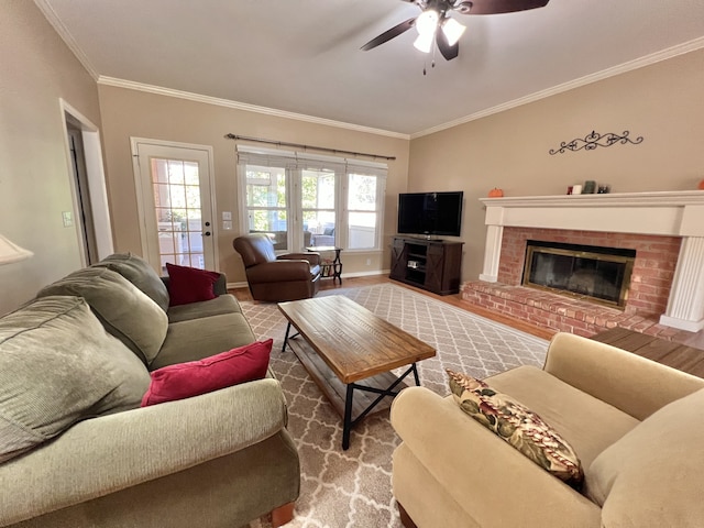 living room with a brick fireplace, hardwood / wood-style floors, ceiling fan, and crown molding