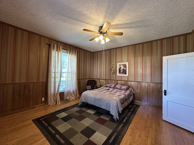 bedroom with a textured ceiling, wood-type flooring, wooden walls, and ceiling fan