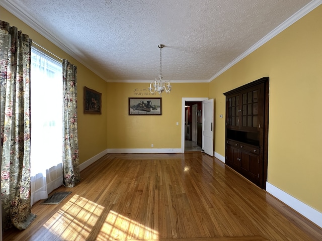 unfurnished dining area featuring light wood-type flooring, a textured ceiling, ornamental molding, and a chandelier