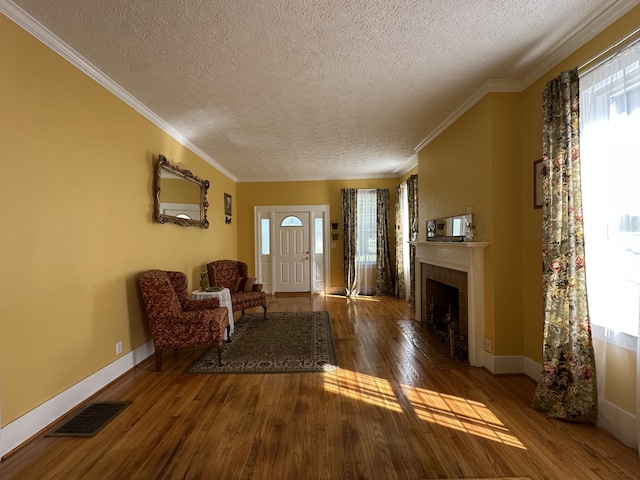 foyer featuring hardwood / wood-style flooring, a tiled fireplace, ornamental molding, and a textured ceiling