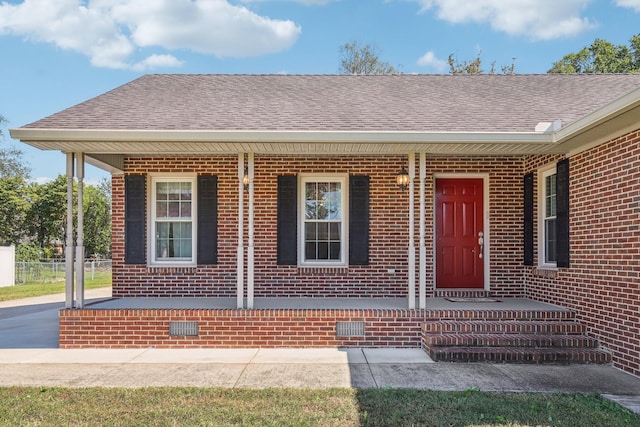 doorway to property featuring a porch, roof with shingles, crawl space, and brick siding