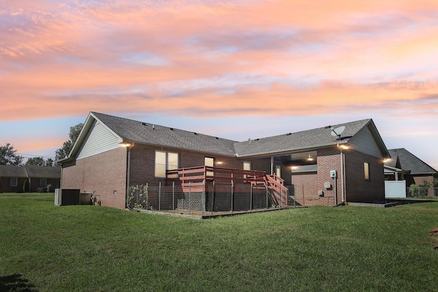 back of house at dusk featuring brick siding, central air condition unit, and a lawn