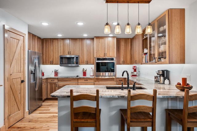 kitchen featuring light stone counters, sink, kitchen peninsula, appliances with stainless steel finishes, and light hardwood / wood-style floors