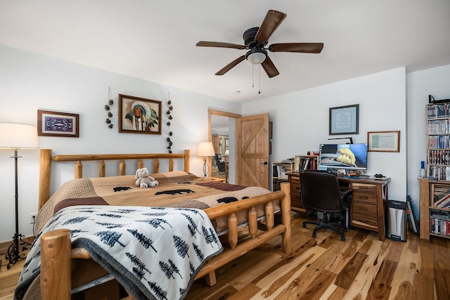 bedroom featuring ceiling fan, light wood-type flooring, and a barn door