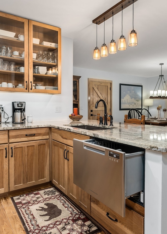 kitchen with light stone countertops, pendant lighting, dishwasher, light hardwood / wood-style flooring, and sink