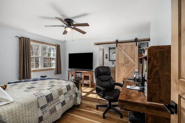 bedroom featuring light hardwood / wood-style flooring, ceiling fan, and a barn door