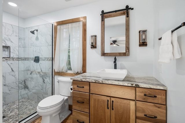 bathroom featuring ceiling fan, vanity, tiled shower, a baseboard heating unit, and toilet