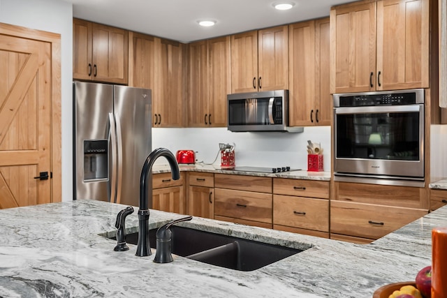 kitchen featuring stainless steel appliances, light stone counters, and sink