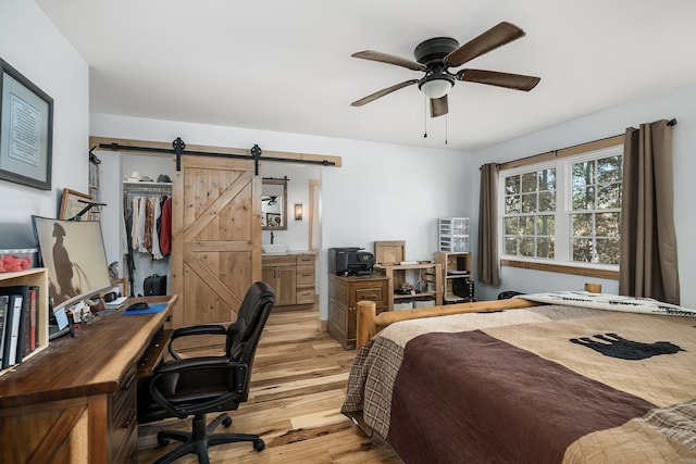 bedroom with a closet, light wood-type flooring, ceiling fan, and a barn door