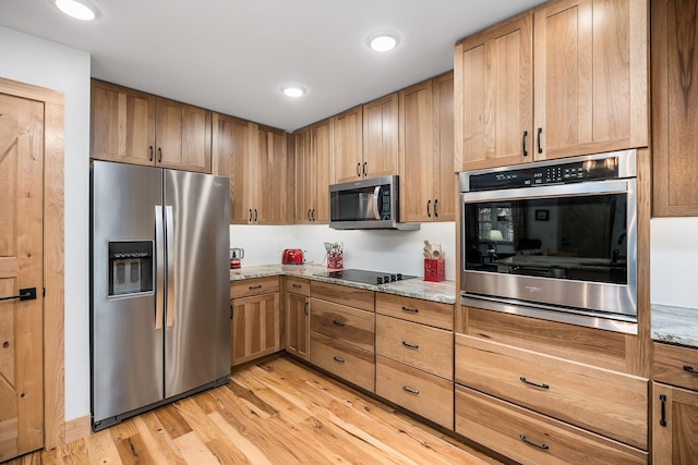 kitchen featuring appliances with stainless steel finishes, light wood-type flooring, and light stone counters