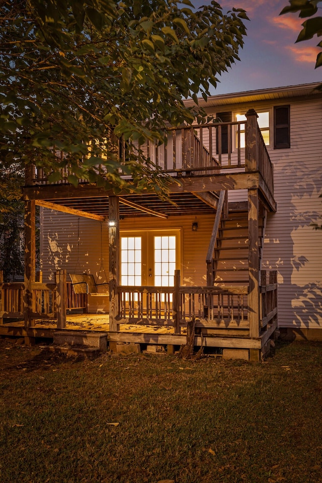 back house at dusk with a wooden deck and a lawn