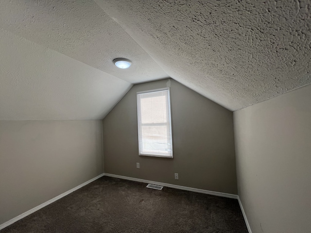 bonus room featuring a textured ceiling, lofted ceiling, and dark colored carpet