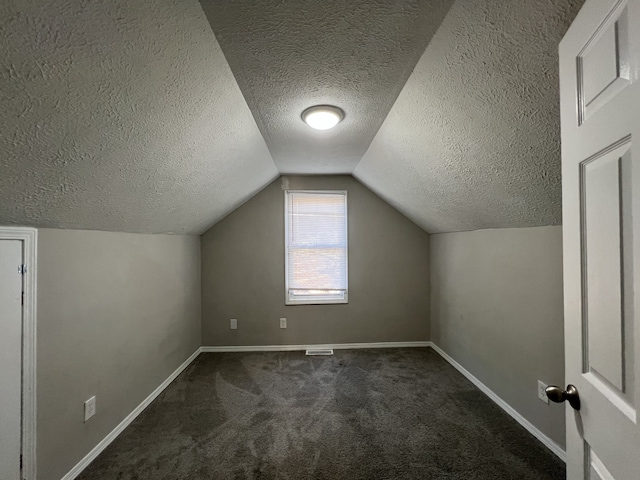 additional living space featuring dark colored carpet, a textured ceiling, and vaulted ceiling