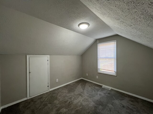 bonus room with a textured ceiling, lofted ceiling, and dark colored carpet