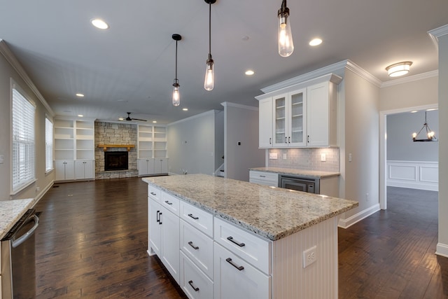 kitchen featuring pendant lighting, a kitchen island, a stone fireplace, white cabinetry, and dark hardwood / wood-style floors