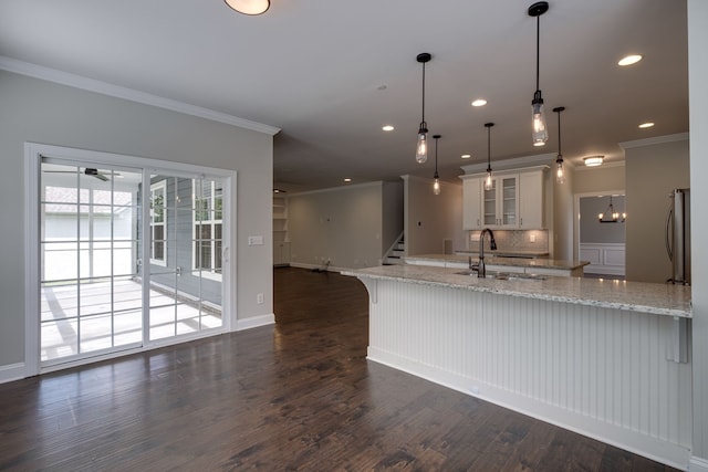 kitchen featuring white cabinetry, dark wood-type flooring, light stone counters, decorative light fixtures, and sink