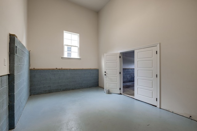 empty room featuring concrete flooring, tile walls, and a towering ceiling