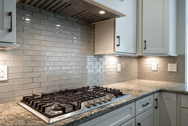 kitchen featuring white cabinets, tasteful backsplash, light stone countertops, stainless steel gas stovetop, and premium range hood