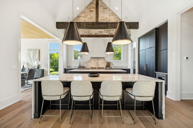 kitchen featuring a large island, light wood-type flooring, light stone countertops, and decorative light fixtures