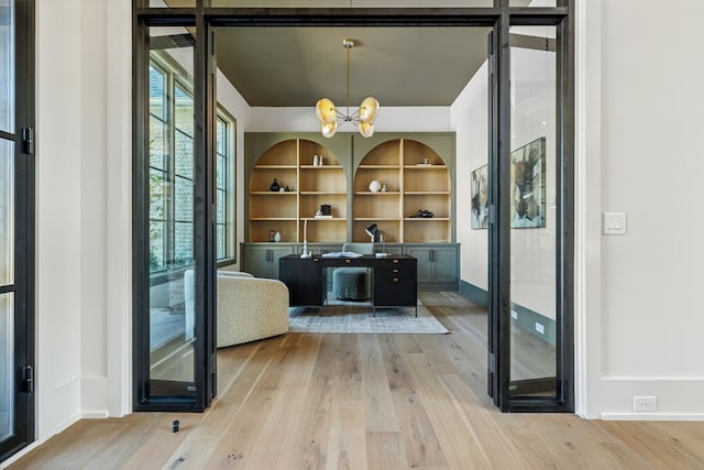 interior space featuring built in shelves, light hardwood / wood-style flooring, and an inviting chandelier