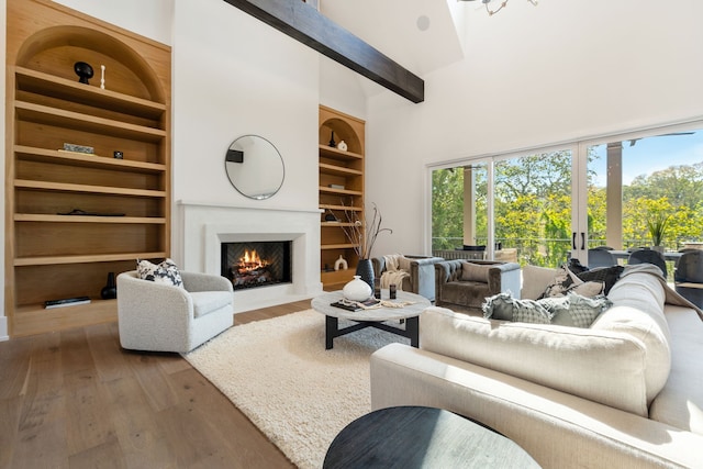 living room featuring built in shelves, a towering ceiling, hardwood / wood-style flooring, and beam ceiling