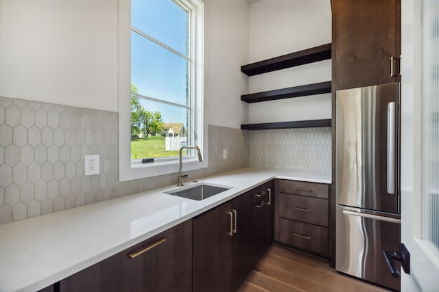 kitchen featuring dark brown cabinets, tasteful backsplash, stainless steel refrigerator, and sink