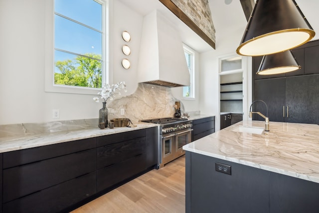 kitchen with premium range hood, range with two ovens, light hardwood / wood-style flooring, light stone countertops, and decorative light fixtures