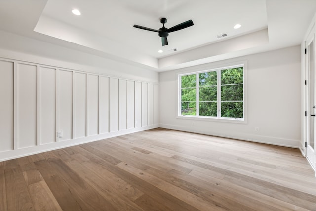 empty room with a raised ceiling, ceiling fan, and light hardwood / wood-style flooring