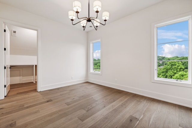 unfurnished room with plenty of natural light, light wood-type flooring, and an inviting chandelier