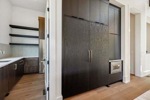 kitchen with decorative backsplash, dark brown cabinets, light hardwood / wood-style floors, and sink