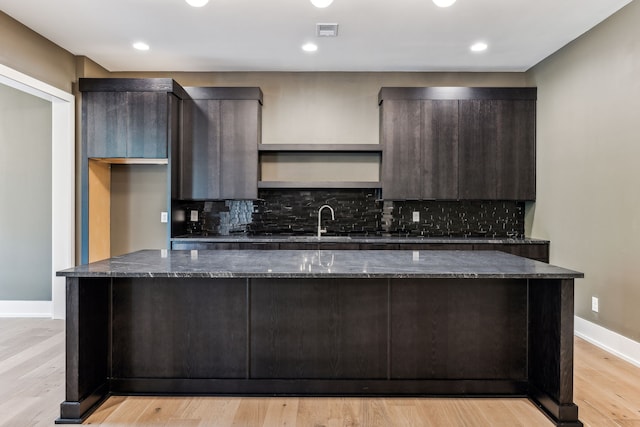 kitchen featuring dark stone countertops, dark brown cabinetry, and light wood-type flooring