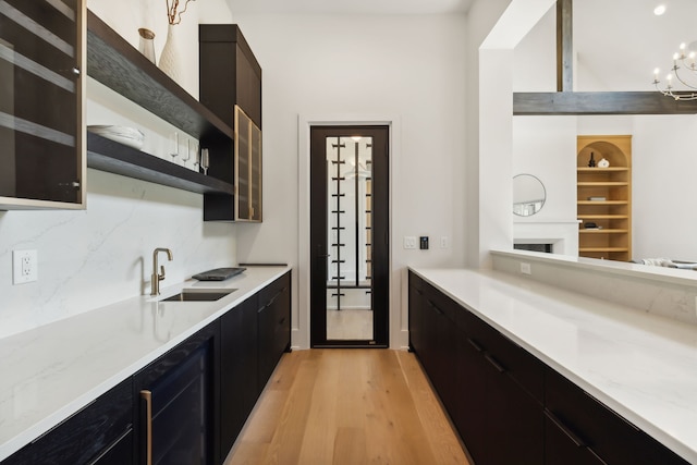 kitchen with backsplash, sink, light wood-type flooring, built in features, and a chandelier