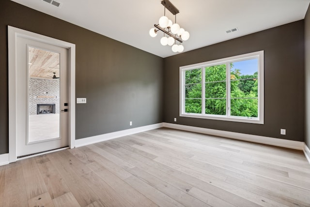 spare room with a fireplace, light hardwood / wood-style flooring, and a chandelier