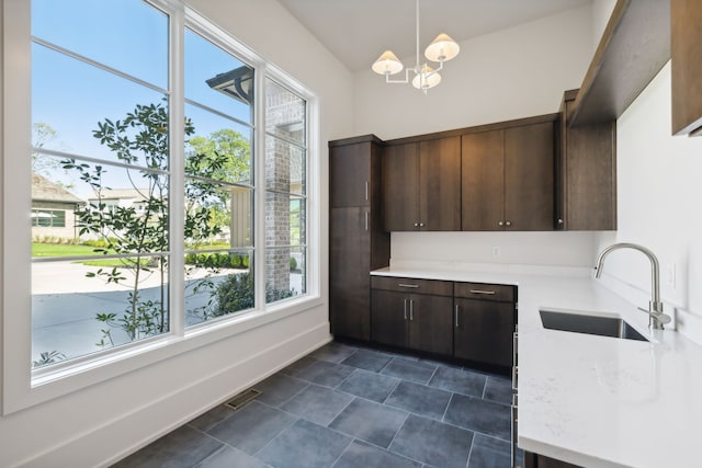 kitchen featuring sink, hanging light fixtures, light stone countertops, a notable chandelier, and dark brown cabinets