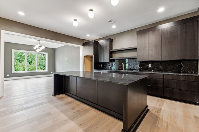 kitchen featuring decorative backsplash, light wood-type flooring, dark stone countertops, a chandelier, and a center island