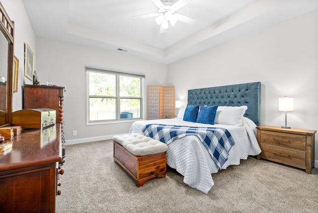 bedroom with a raised ceiling, ceiling fan, and light carpet