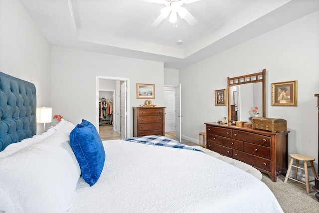 bedroom featuring a spacious closet, ceiling fan, a closet, light carpet, and a tray ceiling