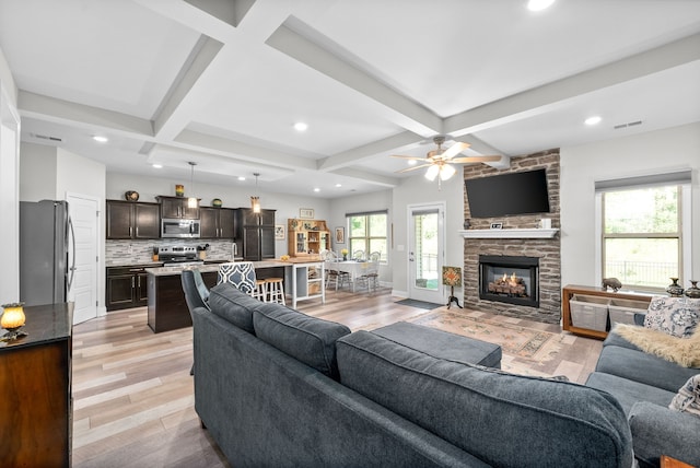 living room with beamed ceiling, ceiling fan, coffered ceiling, light hardwood / wood-style flooring, and a stone fireplace