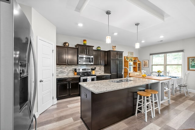 kitchen featuring light hardwood / wood-style floors, dark brown cabinets, stainless steel appliances, hanging light fixtures, and an island with sink