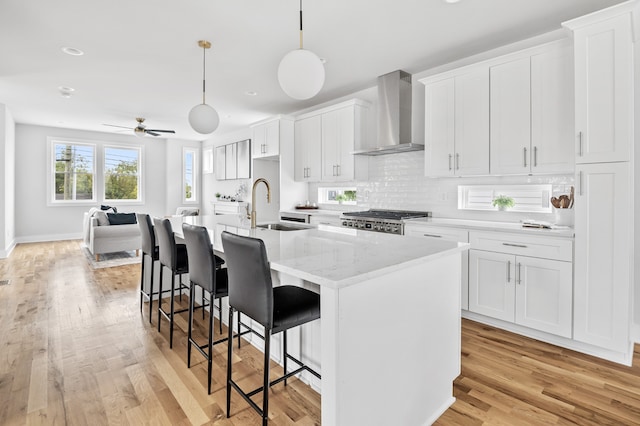 kitchen featuring light hardwood / wood-style floors, wall chimney range hood, an island with sink, and white cabinets