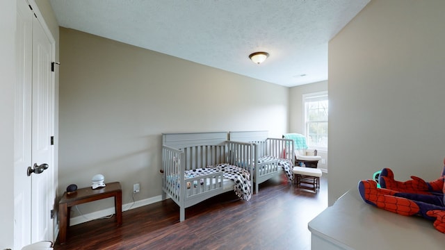 bedroom featuring a nursery area, a textured ceiling, and dark hardwood / wood-style flooring