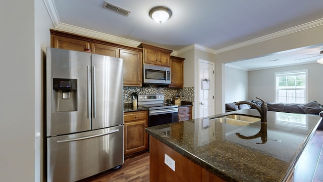 kitchen featuring dark wood-type flooring, a kitchen island with sink, sink, appliances with stainless steel finishes, and ornamental molding