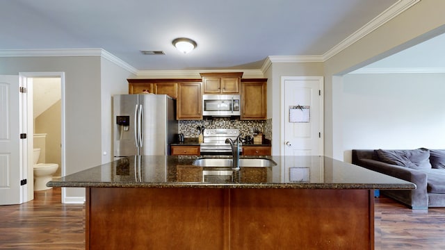 kitchen featuring appliances with stainless steel finishes, ornamental molding, a kitchen island with sink, and dark hardwood / wood-style flooring